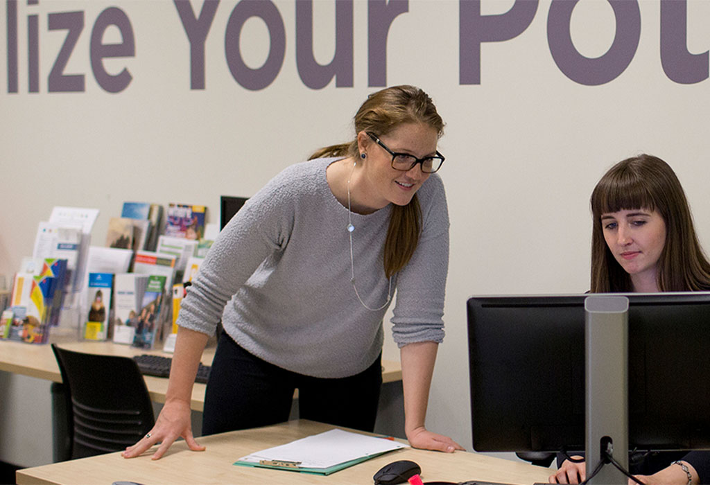 Two post-secondary institution registrar staff look at a computer together.