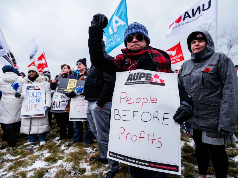 AUPE members at a rally, one member holding a sign that says "people before profit"