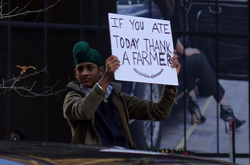 A young Sikh boy holds up a sign at a protest. The sign reads "if you ate today, thank a farmer."