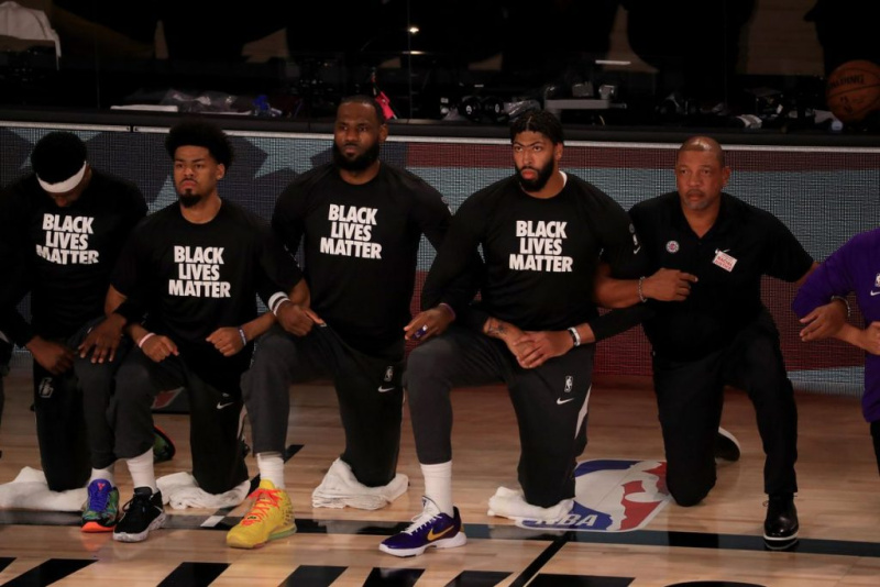 Professional basketball players, including Lebron James, kneel on the court while wearing matching shirts that read "Black Lives Matter."
