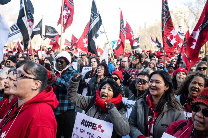 Members at a rally chanting and holding signs and flags.